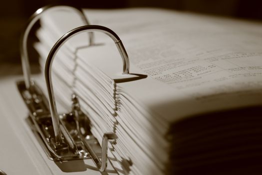Detailed sepia close-up of a binder filled with documents, emphasizing texture.