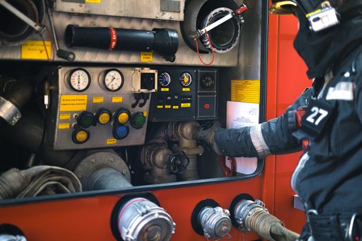 A firefighter in gear adjusting controls on a fire engine during an emergency response.